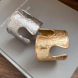 Dettaglio di bracciali a polsino testurizzati oro e argento su un libro grigio.