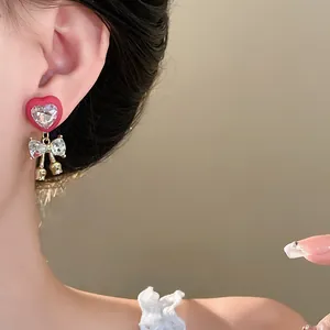 Exquisite close-up of a silver needle earring with red heart and rhinestone bow on ear