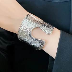 Dettaglio ravvicinato di un bracciale a polsino argento con texture stropicciata e vuoto