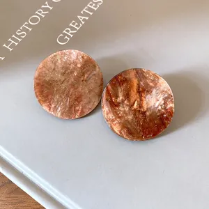 Close-up of round acrylic earrings with brown marble texture and fine glitter