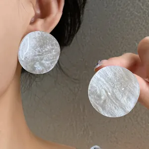 Detailed macro view of white marbled acrylic round stud earrings with subtle glitter finish