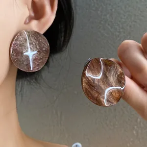 Close-up of brown marble acrylic round earrings showing texture and size on ear