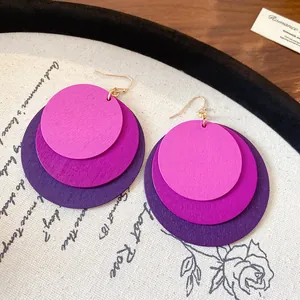 Detail of three-tiered round wooden drop earrings in vibrant purple and pink tones.