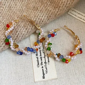 Detalle de pendientes de aro dorados con perlas y cristales de colores sobre fondo texturizado.