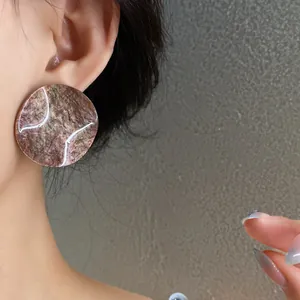 Close-up of large acrylic round stud earrings with brown marble texture on a model