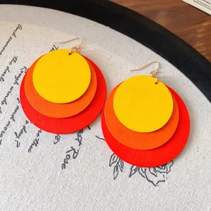 Detailed view of tiered circular wooden drop earrings in yellow, orange, and red tones.