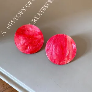 Close-up of pink marbled acrylic round stud earrings with gold glitter flakes.