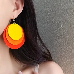 Detailed view of large multi-colored circular wooden layered earrings on model's ear