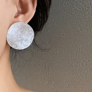 Close-up view of a minimalist white marble acrylic round stud earring worn on ear