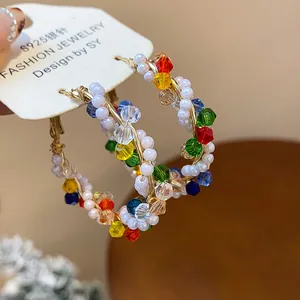 Detalle de pendientes de aro con perlas y cristales de colores en hilo dorado