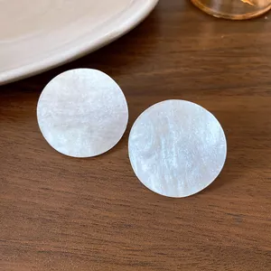 Detailed macro shot of white pearlescent acrylic round stud earrings on a wood background