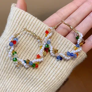 Detalle de pendientes de aro dorados envueltos con cristales de colores y perlas blancas.