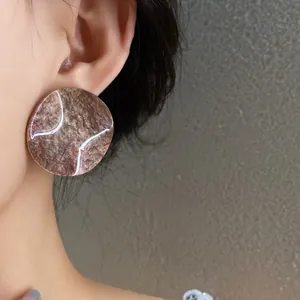 Close-up of French style round acrylic stud earrings with marble texture on ear.