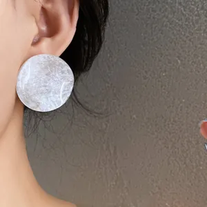 Macro detail showing French style round white marble acrylic stud earrings worn on ear