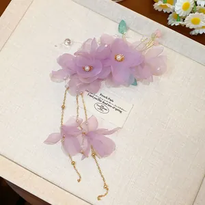 Vue détaillée d'une pince à cheveux fleur en tissu violet avec perles et glands dorés