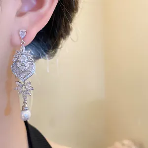 Primo piano di orecchini a foglia e cuore con strass luccicanti e perle pendenti.