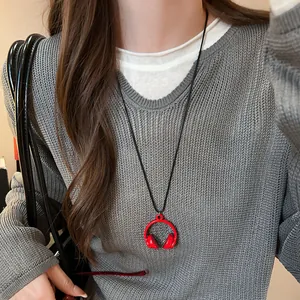 Detail view of a mini red enamel headphone pendant necklace on a grey sweater
