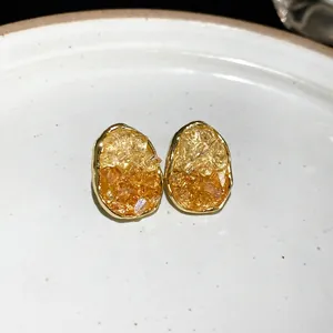 Elegant gold-edged oval stud earrings with amber crushed crystals shown on white plate.