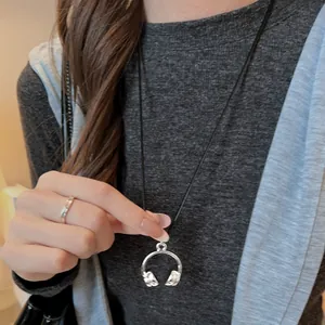 Detailed close-up of a stylish silver headphone pendant necklace worn over a casual grey sweater.