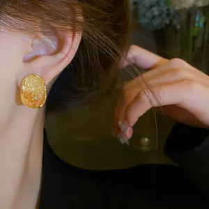 Detailed close-up view of a geometric oval gold earring with amber crystal inlay