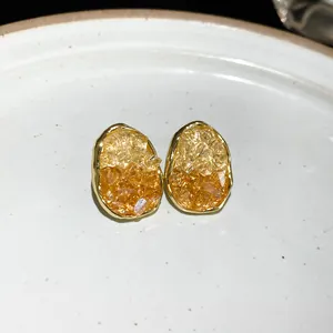 Macro detail of oval stud earrings featuring yellow and orange crushed crystal inlay