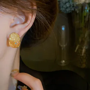 Close-up of elegant oval crystal earrings with textured orange stones and gold trim