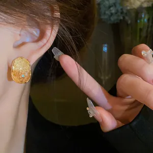 Elegant gold geometric oval earrings with amber crystal texture shown on model