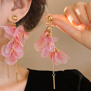 Detailed view of pink gauze flower earrings with long gold dangles on model's ear