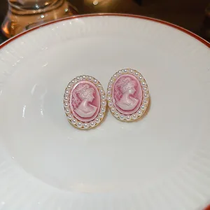 Macro detail of elegant pink cameo stud earrings with white pearl border on ceramic plate.