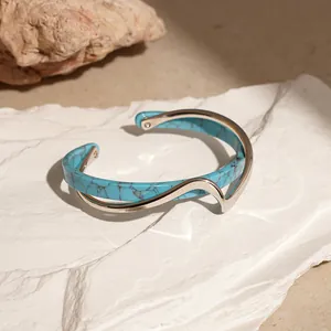Dettaglio di un bracciale a polsino dorato a onda con texture in pietra turchese