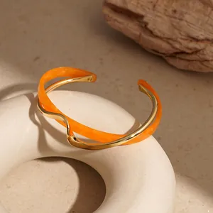 Dettaglio del bracciale rigido in metallo dorato ondulato e acrilico arancione