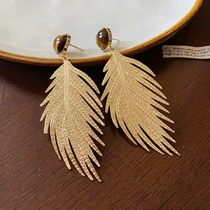 Vintage golden feather leaf earrings featuring round tiger eye stones on wood background