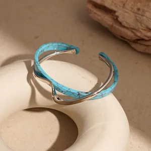 Dettaglio di un bracciale rigido ondulato in metallo dorato e acrilico turchese