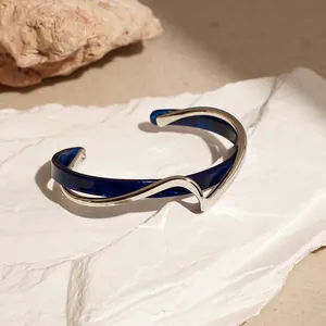 Dettaglio macro del bracciale rigido ondulato in acrilico blu e metallo su pietra bianca