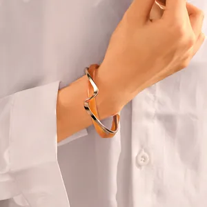 Dettaglio di un bracciale aperto minimalista in metallo ondulato e acrilico ambra sul polso