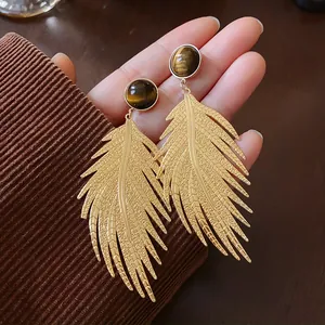 Close-up of gold leaf-shaped earrings with artificial tiger eye stone