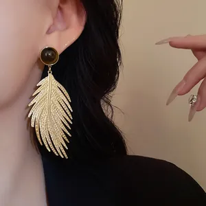 Close-up of gold leaf drop earring with tiger eye stone accent on model's ear.