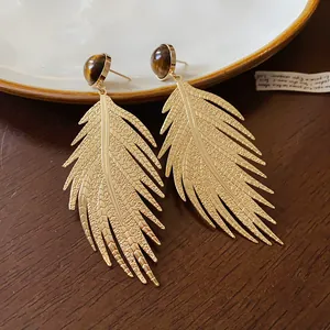 Detailed macro view of golden leaf earrings with tiger eye stone and silver needles