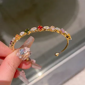 Dettaglio di un bracciale rigido dorato aperto con zirconi cubici multicolori brillanti.