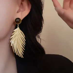 Detailed macro view of golden leaf dangle earrings with faux tiger eye stone stud