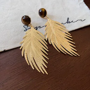 Close-up of golden leaf drop earrings with polished faux tiger eye stone inlay.