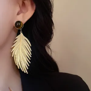 Detail view of elegant golden leaf earrings with tiger eye stone worn on a model's ear