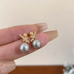 Close-up of gold-plated zircon earrings with elegant grey pearls and cross-knot design