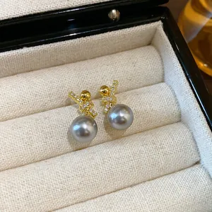 Close-up detail of elegant gold-plated zircon knot earrings with grey pearls