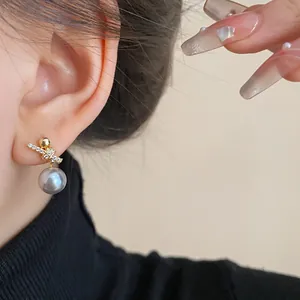 Elegant close-up of a gold-plated zircon knot earring with a grey pearl drop worn on an ear.