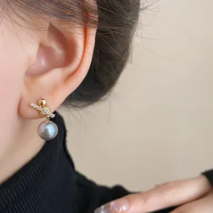 Close-up of elegant gold-plated earrings with zircon cross and grey pearl drop on model