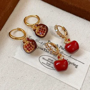 Detailed macro shot of gold plated pomegranate and red apple earrings with zircon inlay