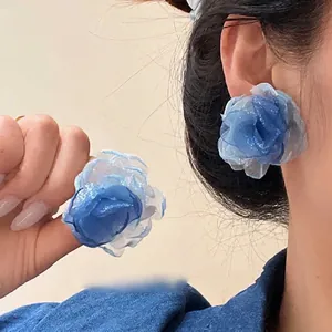 Orecchini a fiore in tulle blu dal design elegante mostrati su orecchio e mano