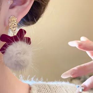 Detailed macro view of a red velvet bow earring featuring a soft grey fur pom-pom on model ear
