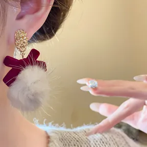 Close-up of fluffy pom-pom earring with red velvet bow and hammered gold stud